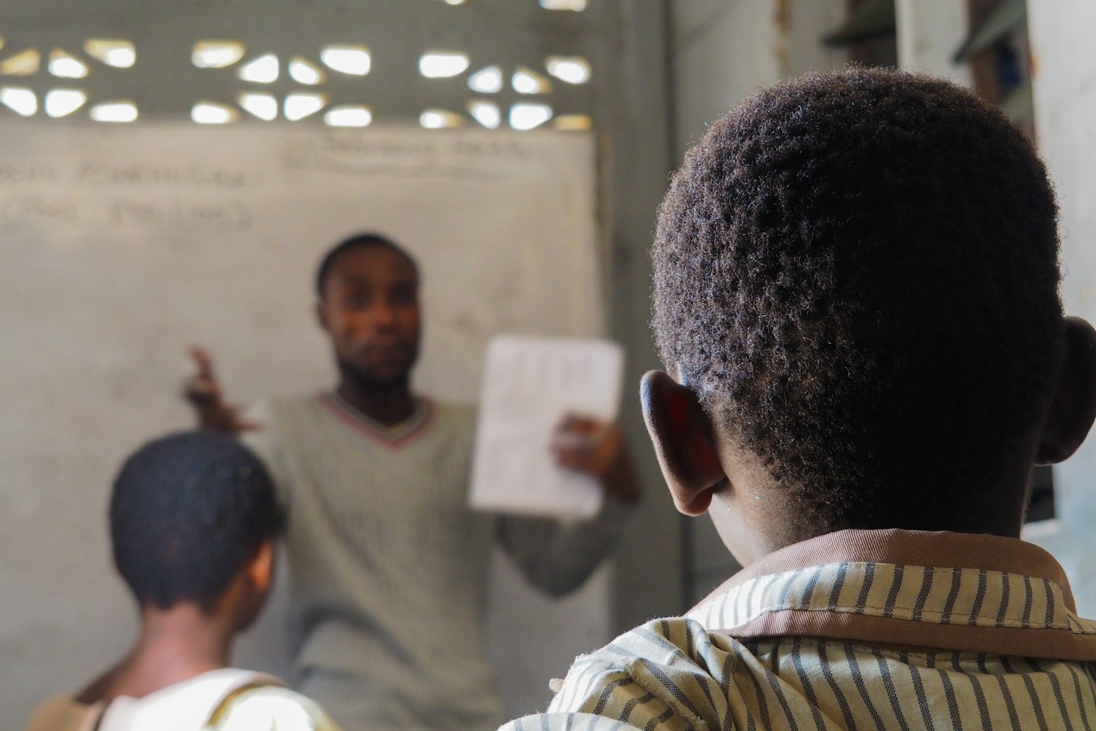 A teacher explaining at the board while holding a paper
